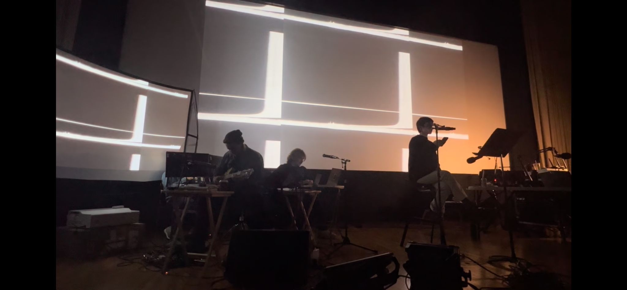 A closer view of musicians and a reader in profile beneath orange and white geometric projections.