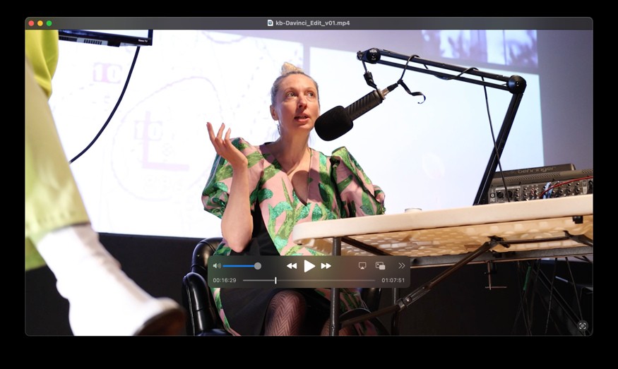 Ash Eliza Smith speaks into a microphone with one hand raised, with projected imagery behind her.